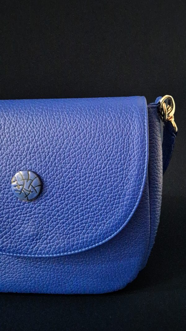 Close-up of the limited-edition sgraffito enamel button on the Cobalta Sigillum leather saddle bag