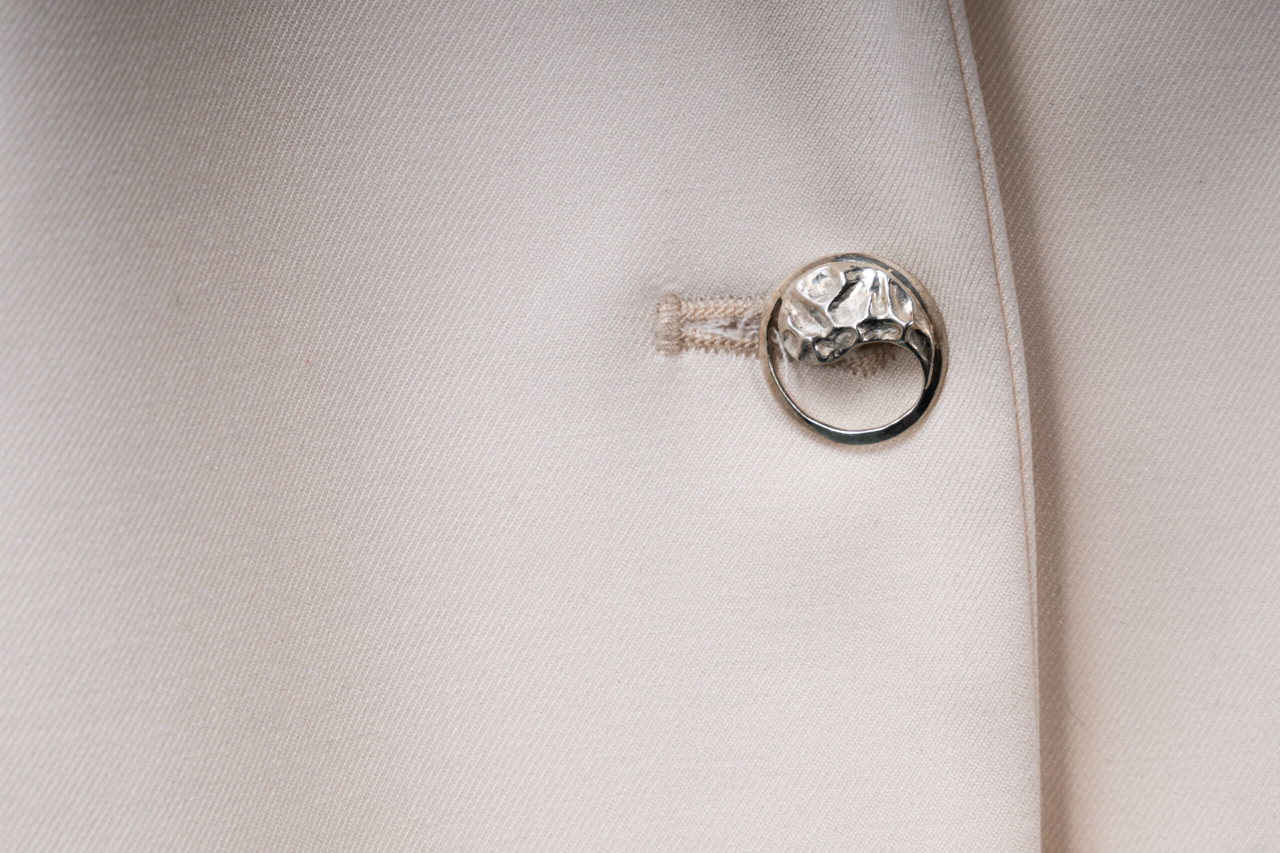 lose-up of the soft ecru fabric and the single Yin-Yang silver button detail on the Argentum Signatum suit jacket.