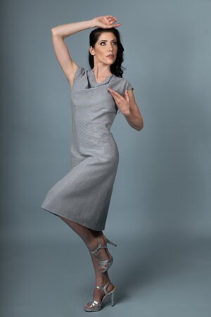 View of the Aurora Aurea draped dress, showcasing its fluid draped neckline, adjustable waist, and soft grey-blue cotton fabric interwoven with gold lurex threads."